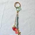 Détail d'un porte-clés plaqué or 18K avec pendentifs fraise et cœur sur tissu blanc - Fraise Transparente Cœur à Carreaux