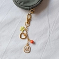 Détail d'un porte-clés doré 18K avec breloques fleurs et abeille sur un porte-monnaie - Abeille Cœur Creux Émail