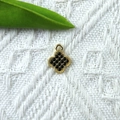 Makro-Detail eines goldenen Kleeblatt-Anhängers mit schwarzen Strasssteinen auf Textil - Schwarz
