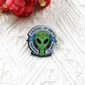 Green alien enamel pin with crescent moon and From Space To Earth banner text - Birth Certificate Alien Style
