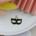 Detail of gold-plated black enamel mask charm with star accent on decorative background - Black