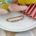 Elegant gold-tone safety pin brooch with decorative spiral accents on a white ceramic plate - Small Brooch