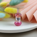 Macro detail of a miniature pink resin bottle charm with a metal loop and orange label - Pink