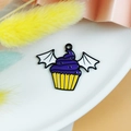 Macro shot of Halloween cupcake bat wing enamel pendant on white plate with flowers - White Bat Wing Cupcake Purple Frosting