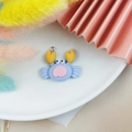 Gros plan d'une breloque crabe en résine bleue et rose avec anneau argenté sur assiette - Crabe