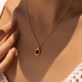 Close-up of a 18K gold-plated necklace featuring an oval red gemstone on a woman's collarbone - Deep Red Oval Gemstone Style (KN0611-1)