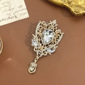 Makroaufnahme einer Vintage-Goldbrosche mit birnenförmigem Kristall und Hohlmuster - Gold