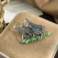 Detailed shot of three vintage giraffe brooches on a beige velvet jewelry box - Silver