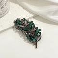 Dettaglio spilla vintage a foglia con cristalli verde scuro e grigio fumo su metallo scuro - Verde