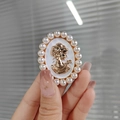 Vue macro de la broche camée vintage avec relief doré et bordure de perles blanches - Style de Broche / Blanc