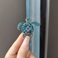 Elegante spilla a tartaruga dorata con strass blu scintillanti tenuta in mano - Tartaruga