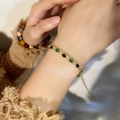 Gouden armband met groene en zwarte kattenoogstenen, gedragen op een vrouwenpols - Goud