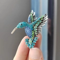 Elegante spilla a forma di colibrì con strass blu e verdi in posa di volo dinamico - Doppio Blu