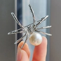 Silver spider brooch with white pearl and sparkling crystals held to show size - White