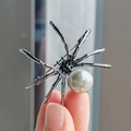 Gothic black spider brooch with large white pearl and rhinestones held by hand - Black