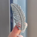 Vista macro de un broche de pluma plateado con brillantes pedrería sostenido en la mano - Broche de Pluma (XZ0338-1)