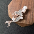Spilla a sirena in oro rosa con cristalli bianchi e perle su un espositore di legno - Oro rosa