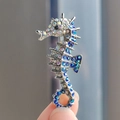 Broche de caballito de mar plateado con diamantes azules en una vista de mano realista - Azul