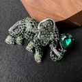 Detailed close-up of elephant brooch with green crystals and rhinestones on black background - Green