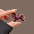 Exquisite horse brooch with red enamel and golden accents held by fingers - Lucky Red Horse Brooch