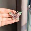 Gouden vlinderbroche met paarse strassteentjes en roze stenen in de hand - Paars