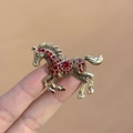 Golden horse brooch with red rhinestones and vintage texture shown on fingertips - Enamel Steed Brooch Red