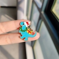 Spilla in smalto dinosauro di Natale blu con cappello di Babbo Natale e regalo - Dinosauro di Natale Blu (XZ0530-1)