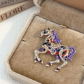 Close-up of golden horse brooch with zircon inlay and colorful enamel in a gift box - Purple