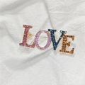 Broche lettre LOVE dorée avec strass colorés sur fond de tissu blanc élégant - LOVE