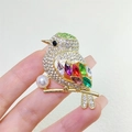 Primer plano detallado de un broche de urraca colorido con cristales y una perla - Dorado