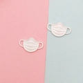 Detailed view of two off-white matte mask-shaped alloy charms for DIY jewelry making - White