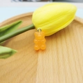 Detailed close-up of a translucent orange resin gummy bear pendant on a light wood tray - Orange