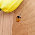 Enamel acorn pendant charm in yellow and black with gold ring on wooden background - Pine Cone