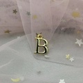 Macro shot of gold-plated letter B pendant on a dreamy pink sequined mesh background - Letter B