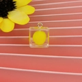 Dettaglio di un ciondolo a cubo in resina con sfera gialla interna e anello in metallo - Stile Cubo con Pom Pon / Giallo