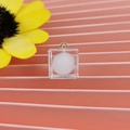 Primo piano di un ciondolo quadrato in resina trasparente con pompon bianco e anello d'oro - Stile Cubo con Pom Pon / Bianco