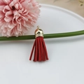 Detail of red faux suede tassel with a gold metal cap hanging for DIY jewelry crafts - Red