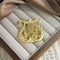 Detalle macro del broche de arpa de oro mate vintage sobre fondo de partitura musical - Broche de Arpa Metálico Liso