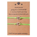 Close-up of handmade woven paw print charm bracelets on a pet memorial card - Green Cord