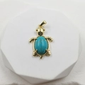 Golden turtle pendant featuring a turquoise stone inlay on a white pedestal display - Turquoise Pendant