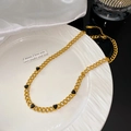 Gros plan du bracelet en chaîne dorée avec cinq pendentifs cœurs noirs sur un plat blanc - Collier avec Cinq Coeurs Noirs (X2179)