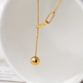 Μινιμαλιστικό χρυσό κολιέ σε σχήμα Y με σφαιρικό μενταγιόν σε κεραμική επιφάνεια - Χρυσό