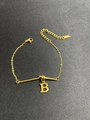 Close-up of gold titanium bracelet with capital letter B pendant on a textured surface - Letter B