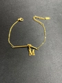 Makroaufnahme: Vergoldetes Edelstahl-Armband mit Buchstabe M und Stab-Anhängern - Buchstabe M