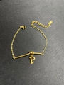 Detail eines Gold-Titan-Armbands mit Buchstaben-P-Anhänger und Metallstab auf dunklem Grund - Buchstabe P