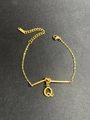 Detail eines goldenen Edelstahlarmbands mit Knoten-Design und Buchstabe-Q-Anhänger - Buchstabe Q