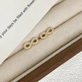 Close-up of gold-plated infinity stud earrings with micro-paved zircons in a jewelry box - Stud Earrings / Gold