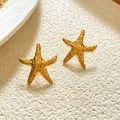 Macro shot of gold starfish earrings with textured hammered finish on white surface - Starfish Shape / Gold Starfish Style
