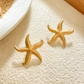 Macro detail of starfish stud earrings with a textured gold finish on a beach sand background - Sea Star Shape / Gold Pearl Texture Starfish Stud Earrings