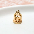 Macro shot of gold-plated hollow birdcage charm with hanging loop and dot texture - Birdcage Style